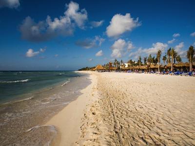 Breiter Sandstrand mit Palmen und blauen Liegestühlen unter blauem Himmel mit Wolken