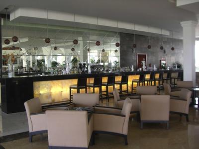 Area lounge dell'hotel moderna con poltrone beige e un bar illuminato con sedie alte.