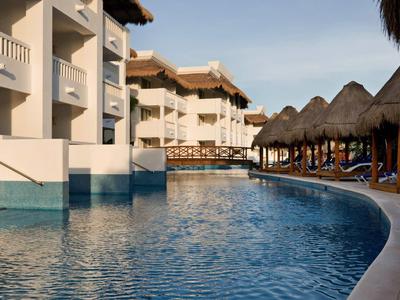 Hotel mit Außenpool und Blick auf Liegestühle unter Strohdächern