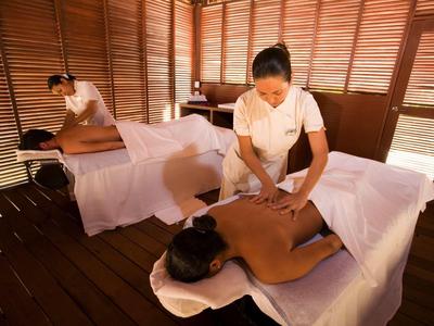 Due donne ricevono massaggi in una spa con pareti in legno e luce soffusa.