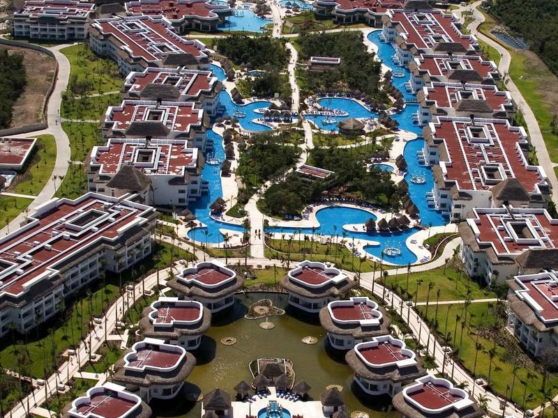 Vista aerea di un grande resort con più piscine e vista sul mare sullo sfondo.