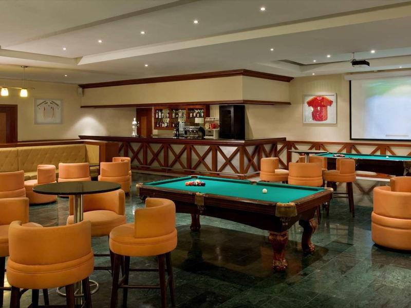 Lounge dell'hotel con tavolo da biliardo, poltrone arancioni e grande schermo per presentazioni o film.
