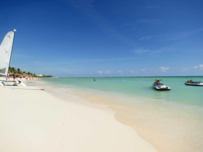 Spiaggia di sabbia bianca con barca a vela e due moto d'acqua sul mare turchese sotto il cielo azzurro