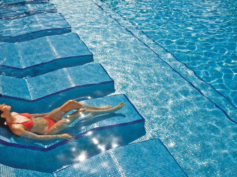 Donna rilassata su lettini integrati nell'acqua limpida della piscina