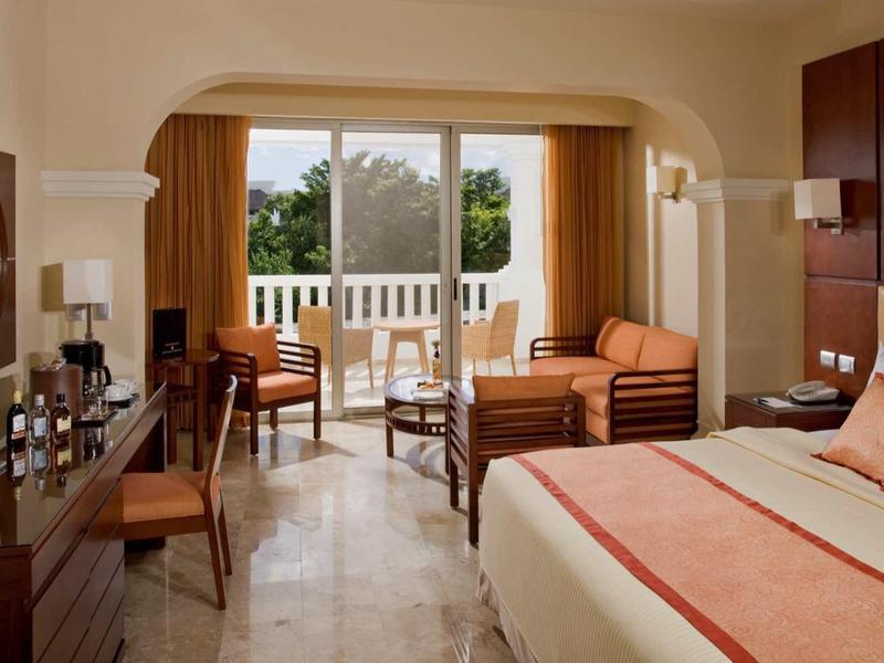 Camera d'hotel accogliente con balcone, due poltrone, scrivania e TV.