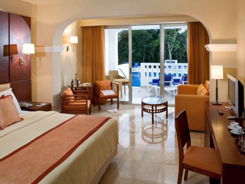 Elegante camera d'hotel con letto grande, zona salotto e balcone che si affaccia sul verde.