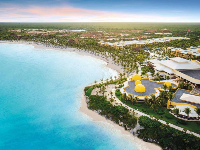 Vista aerea di un resort tropicale con spiaggia di sabbia bianca e acqua azzurra limpida.