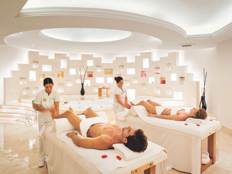 Tre persone ricevono massaggi rilassanti su lettini in una spa luminosa.
