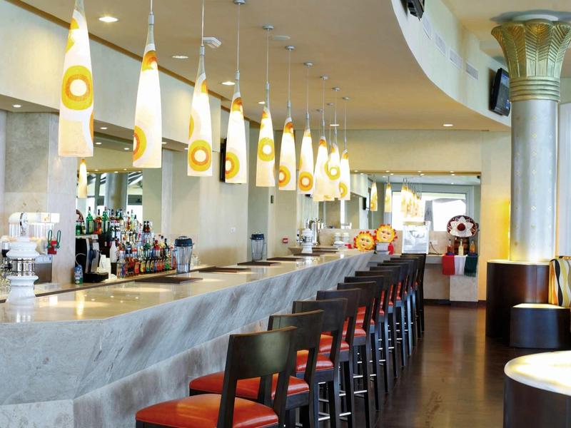 Bar dell'hotel moderna con sedie alte e lampade a sospensione gialle sopra il bancone.