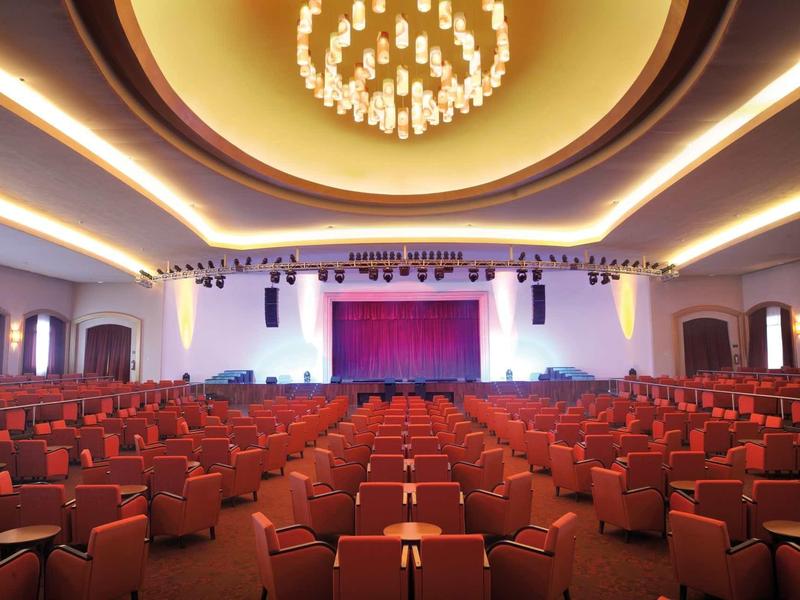 Grande sala teatrale con sedili rossi e lampadario illuminato al soffitto.