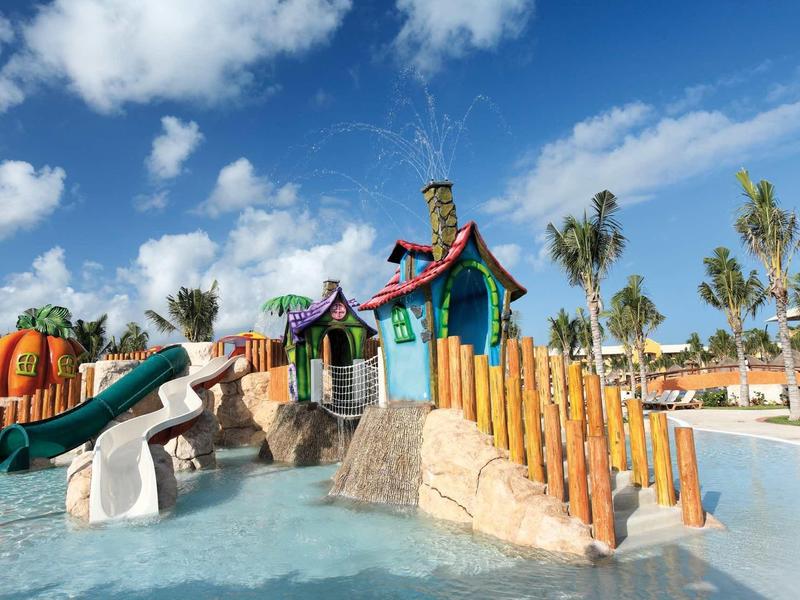 Area giochi acquatica colorata con scivoli e strutture sotto un cielo azzurro in un resort.