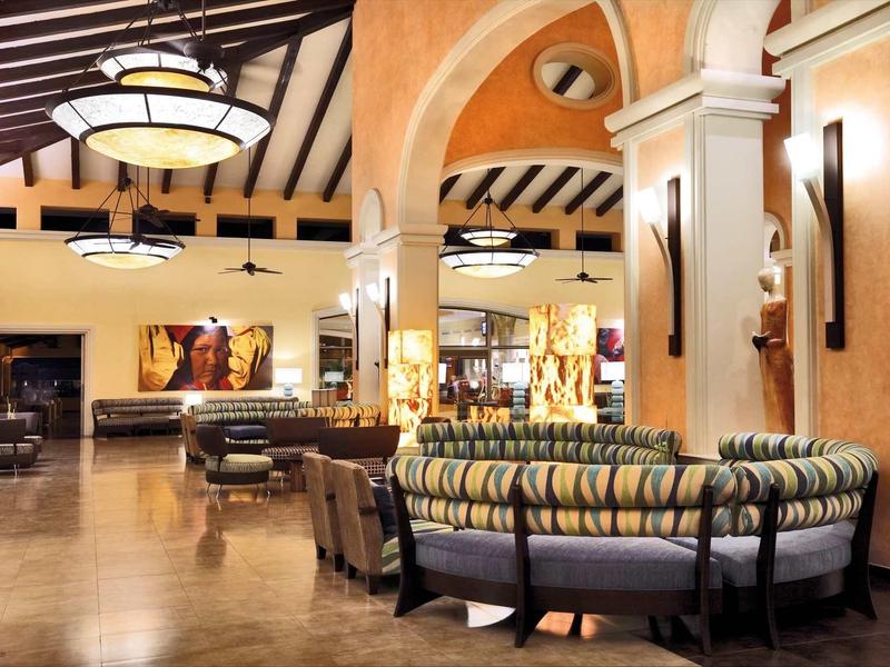 Interno di una hall di hotel con aree salotto rotonde, luci a soffitto e colori caldi.