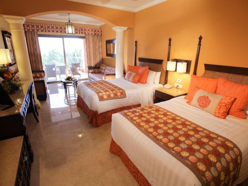 Camera d'hotel con due letti matrimoniali, accenti arancioni e balcone con vista mare.