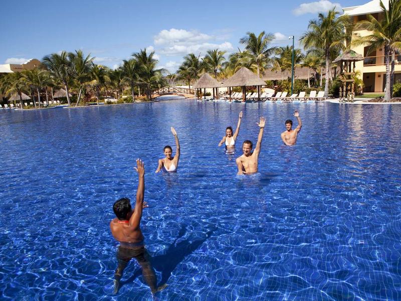 Sei persone giocano a pallamano in una grande piscina blu dell'hotel sotto un cielo sereno.