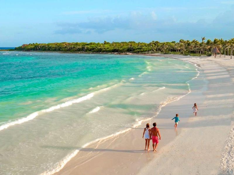 Spiaggia con sabbia bianca, mare turchese e poche persone che camminano sulla riva.