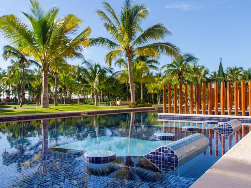 Piscina con angolo di piastrelle a mosaico blu e palme sullo sfondo sotto un cielo soleggiato.