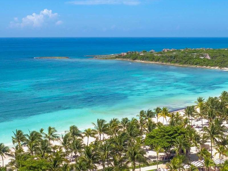 Vista di una spiaggia tropicale con palme, sabbia bianca e acqua azzurra limpida.