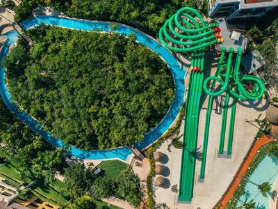 Vista aerea di più scivoli d'acqua verdi accanto a un fiume lento in un resort tropicale.