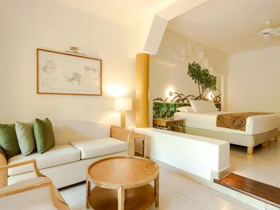 Modern eingerichtetes Hotelzimmer mit Sofa, Bett und Pflanzen in warmem Farbschema.