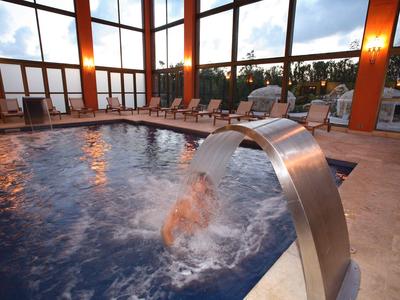 Vnitřní bazén s vodním prvkem a lehátky ve velké světlé místnosti s panoramatickými okny