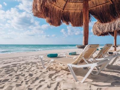 Lettini vuoti con ombrelloni di paglia su una spiaggia sabbiosa soleggiata vicino al mare.