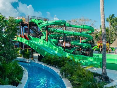 Complesso di scivoli d'acqua verdi con molte curve all'aperto, circondato da piante tropicali.