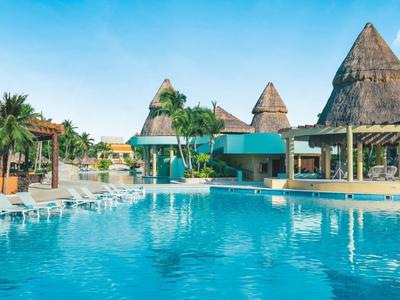 Grande piscina dell'hotel con padiglioni con tetto di paglia esotici e palme sotto un cielo limpido.