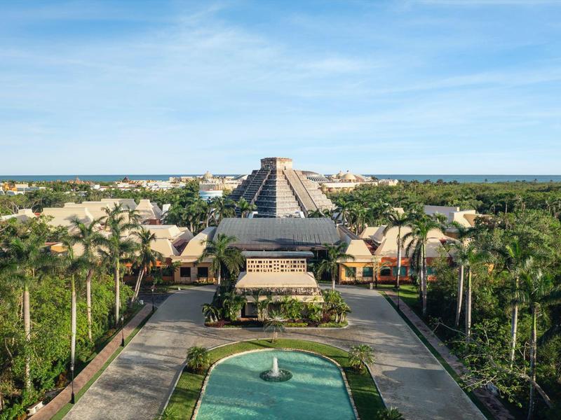 Vista di un resort di lusso con edificio principale a forma di piramide e verde rigoglioso intorno.