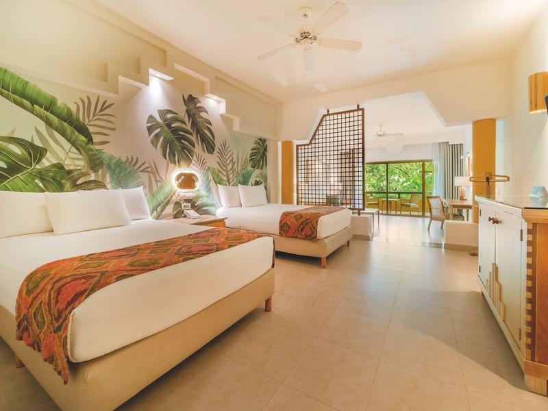 Camera d'hotel luminosa con due letti e grande vetrata che si affaccia sulla terrazza.