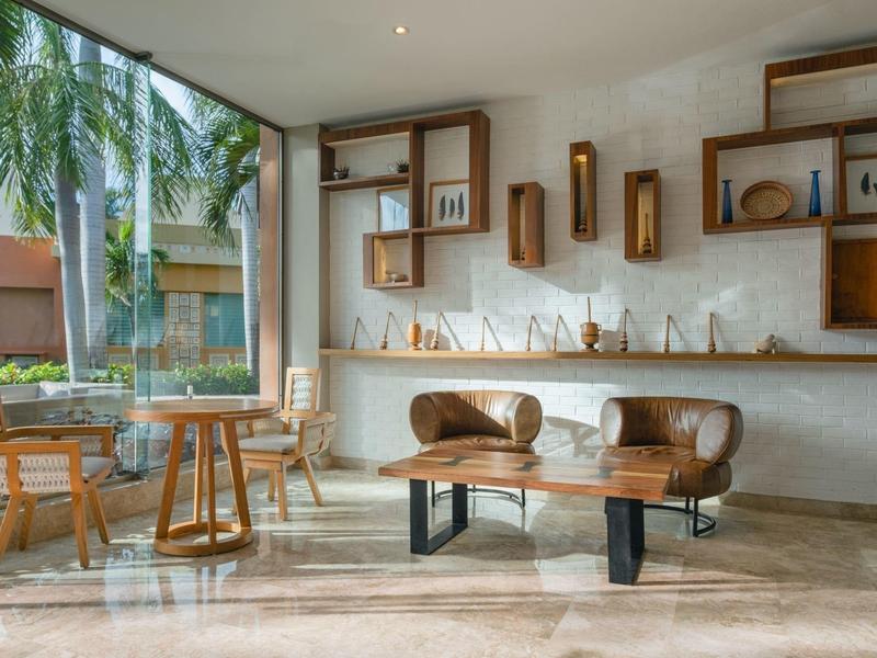 Lobby di hotel moderna con divano in pelle, sedie in legno e grandi finestre con vista sulle palme.