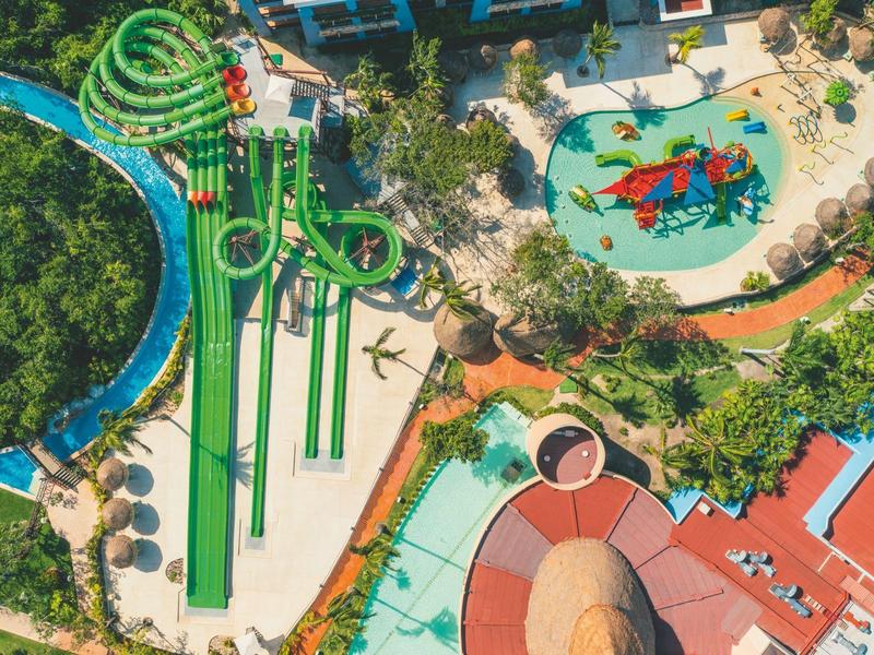 Vista aerea di un parco acquatico con scivoli, piscina e area giochi circondati da alberi.