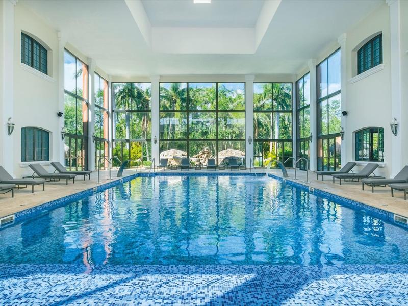 Piscina coperta con grandi finestre e lettini in un hotel moderno.