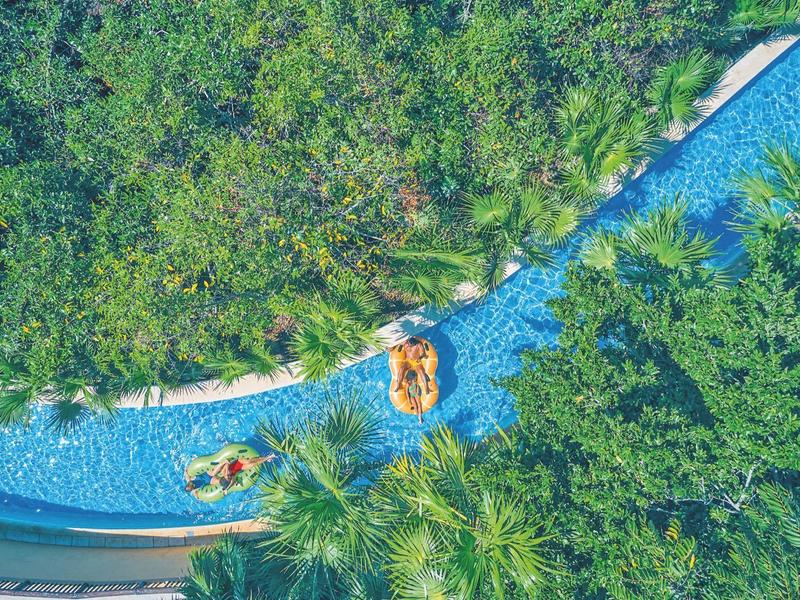 Vista dall'alto di una piscina tortuosa bordata da palme con persone su gonfiabili