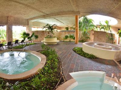 Area spa esterna con vasca idromassaggio rotonda, piante e lettini sotto una copertura.