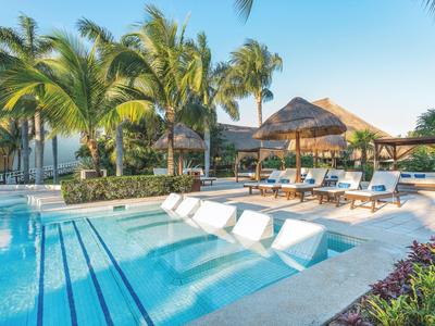 Einladender Pool mit Liegen, Palmen und Sonnenschirmen bei klarem Himmel.