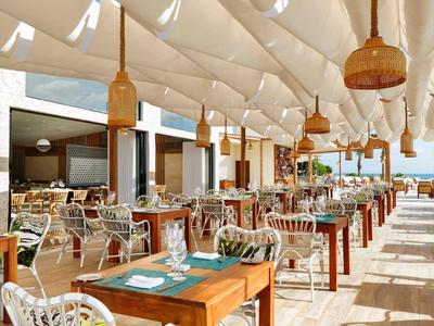 Ristorante all'aperto con tavoli in legno e sedie bianche sotto un tendone chiaro.