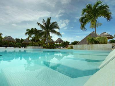 Piscina turchese circondata da palme sotto un cielo parzialmente nuvoloso.