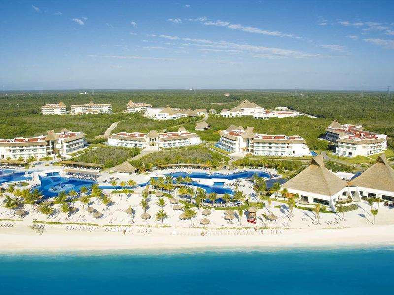 Resort sulla spiaggia con più edifici, piscine e palme lungo la costa sotto un cielo azzurro.