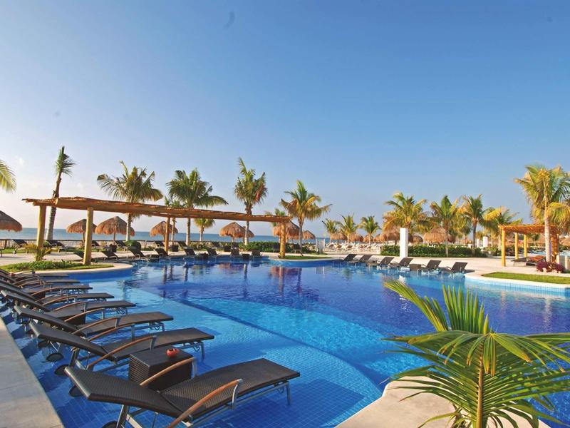 Grande piscina all'aperto con lettini e ombrelloni sotto palme in una giornata soleggiata.