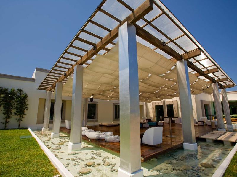 Area esterna moderna coperta con sedute circondata da acqua e prati.