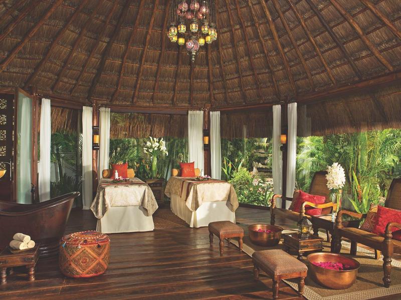 Salotto accogliente all'aperto con pavimento in legno, sedie in vimini, divani, piante e tetto di paglia.