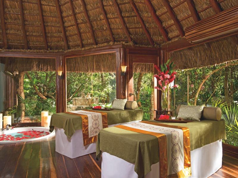 Accogliente sala spa con lettini da massaggio e vasca fiorita circondata da verde.