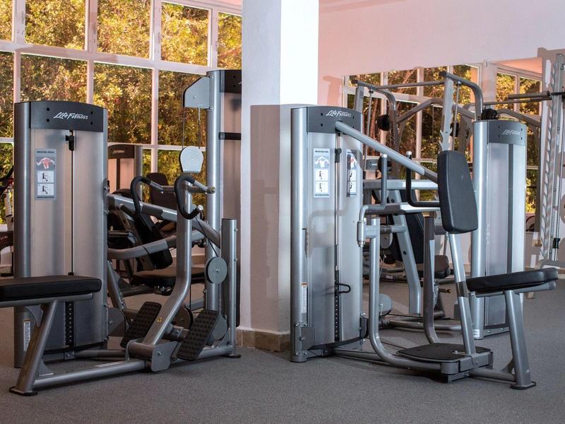 Palestra moderna con macchine per pesi e grandi finestre con vista sugli alberi.