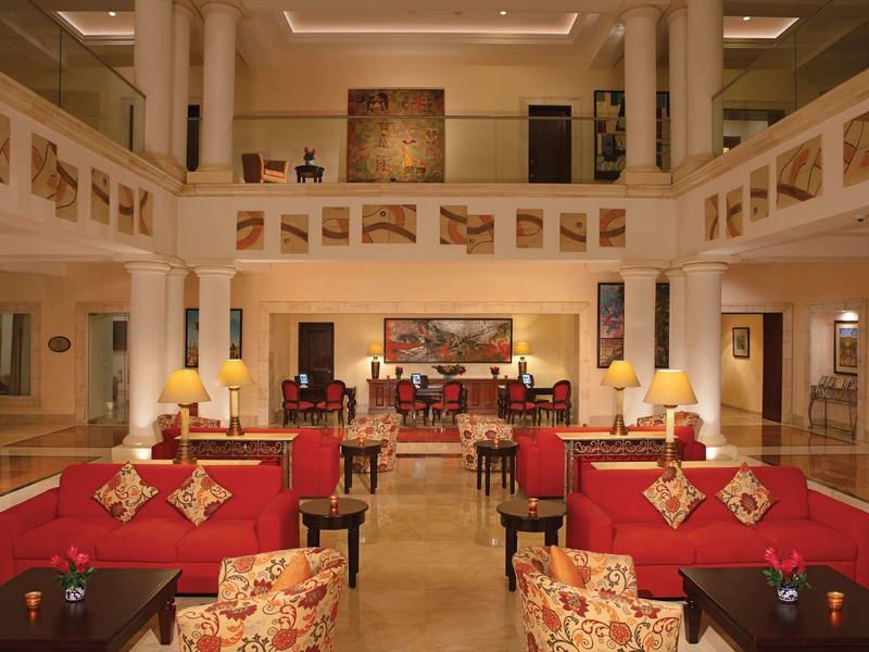 Ampio atrio d'hotel con divani rossi, poltrone decorate e illuminazione calda.