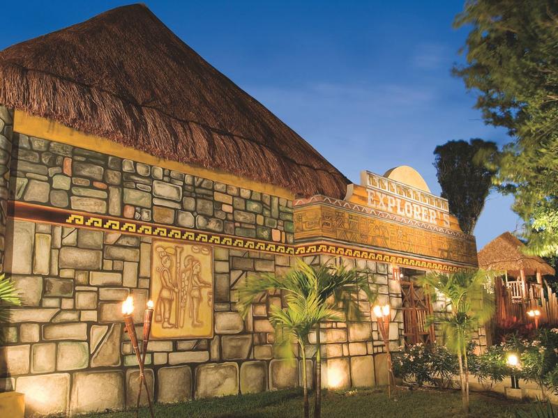 Edificio in pietra con tetto in paglia illuminato al crepuscolo con piante tropicali intorno.