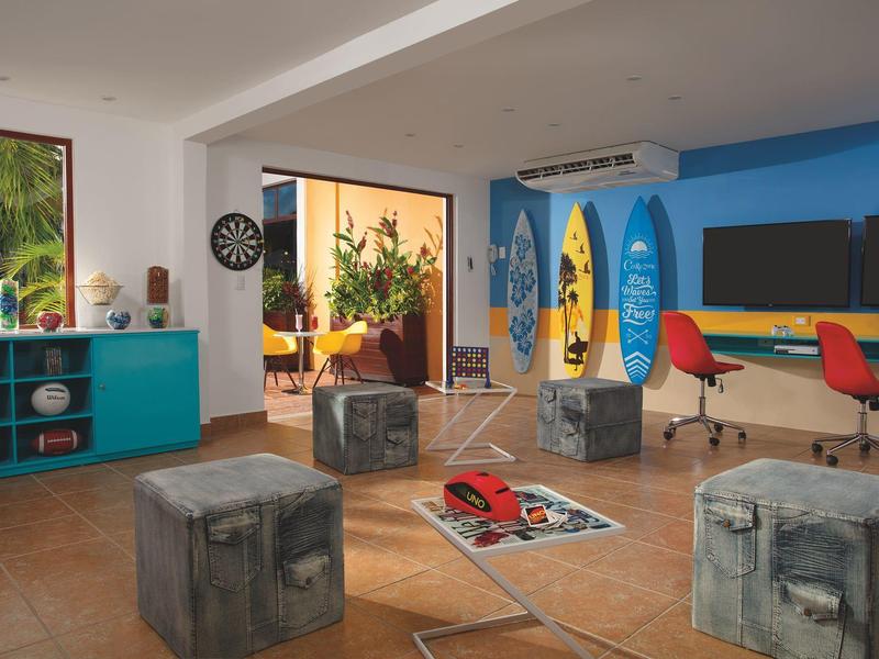 Stanza moderna a tema spiaggia con tavole da surf, colori vivaci e pouf vicino a una grande finestra.