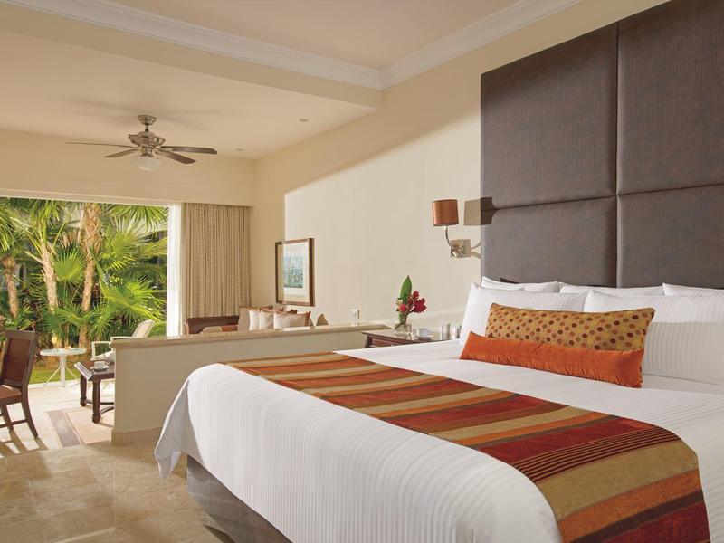 Ampia camera d'hotel con letto grande, zona salotto e balcone aperto con vista sul verde.