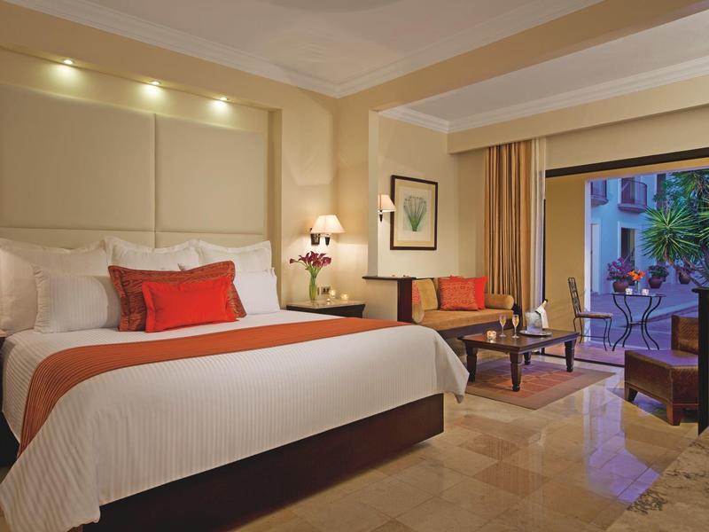 Camera d'hotel accogliente con letto grande, luci da comodino, zona soggiorno e balcone.