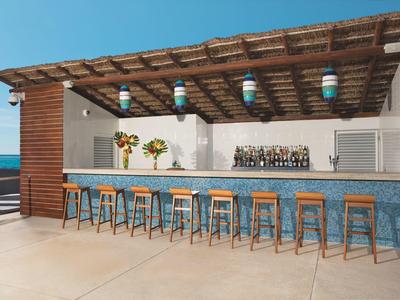 Outdoor bar with wooden stools under a pergola overlooking the sea.
