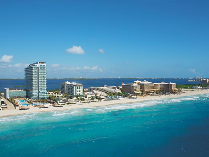 Coastline with white sandy beaches and hotels along turquoise sea under clear sky.
